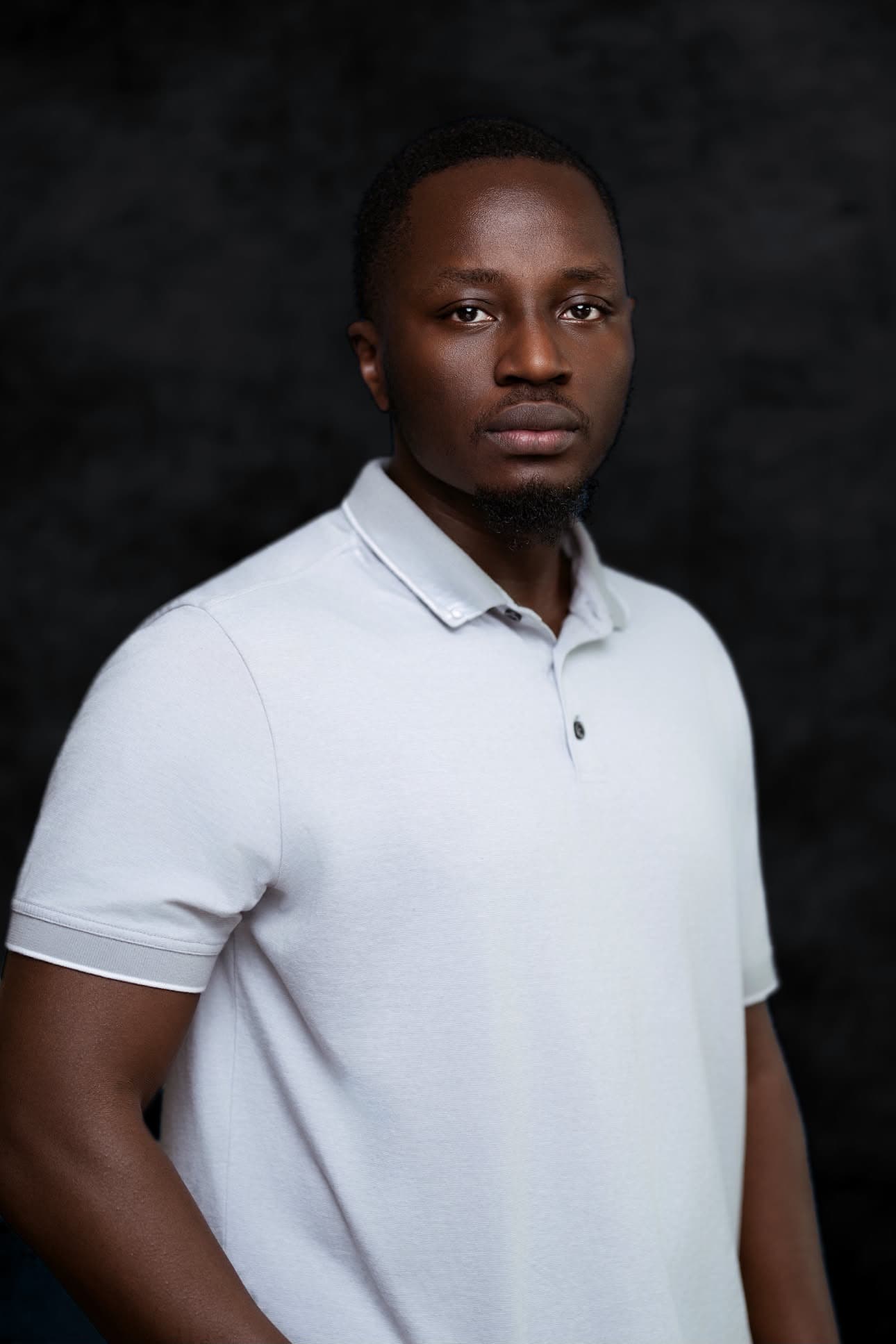 Studio portrait of Arbogaste Steven in a white polo shirt against a dark backdrop